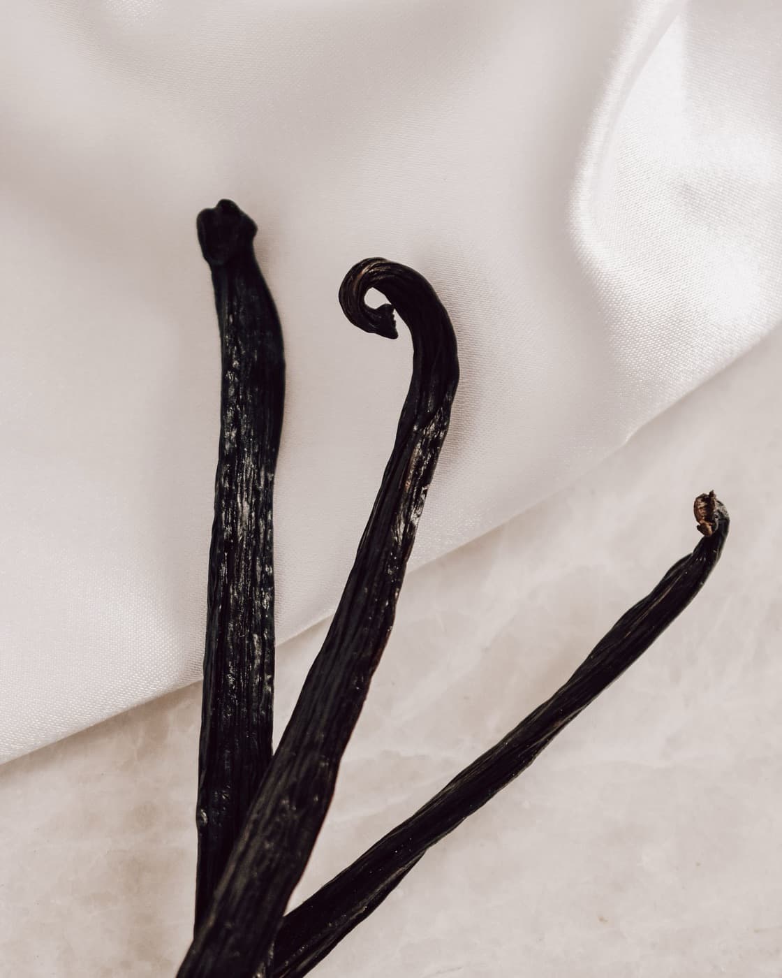 Three cured vanilla beans, dark and supple, on white cloth